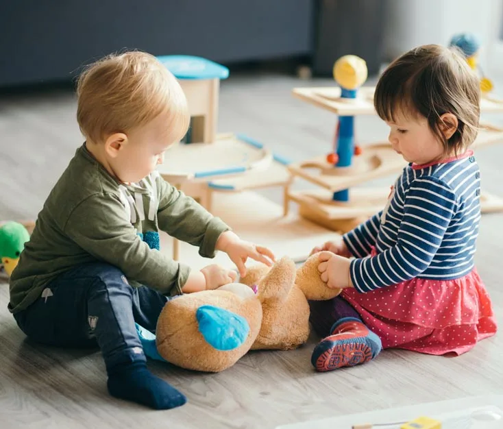Two toddlers playing together with a stuffed toy